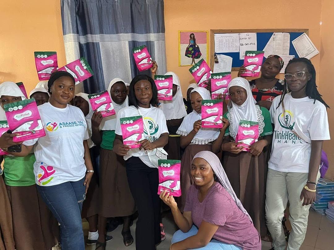 Schoolgirls holding packs of sanitary pads with Asaase Yaa volunteers